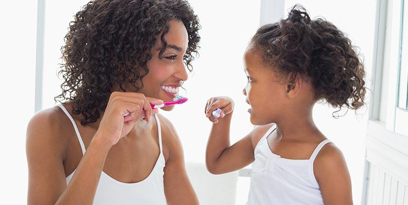 a mother and young daughter brushing their teeth together