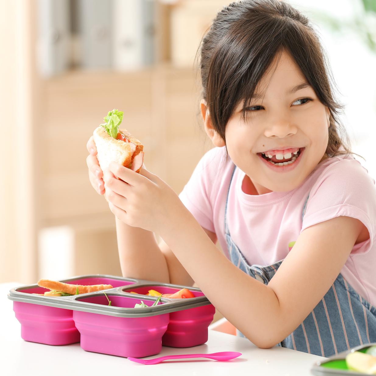 Child smiling while enjoying healthy packed lunch.