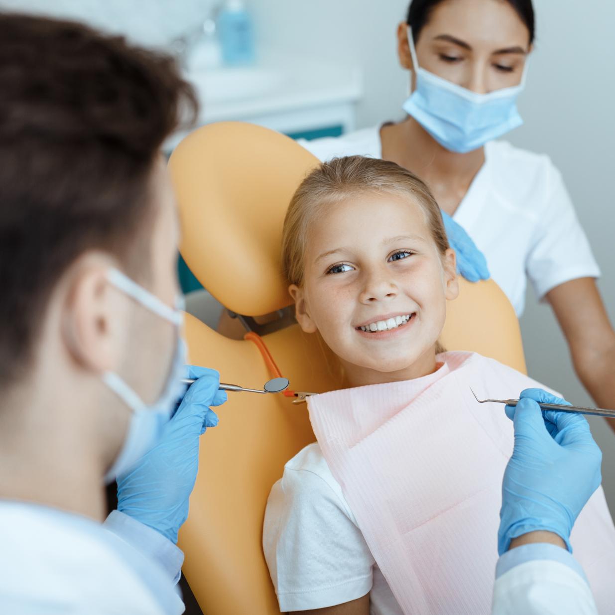 Happy child at dental office receiving care from dentist and hygienist. 