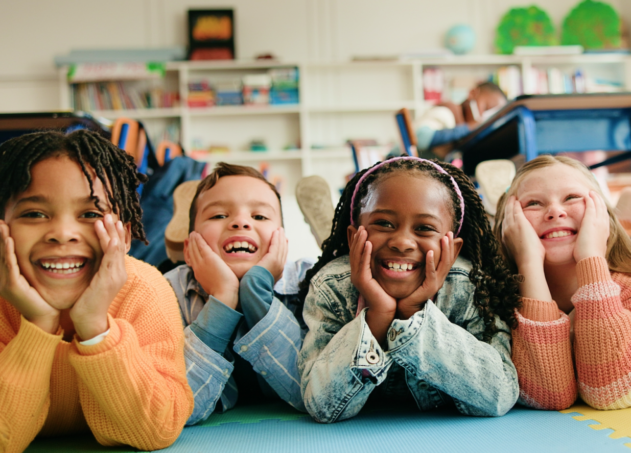 Kids laying together on the floor at school smiling with their heads in their hands