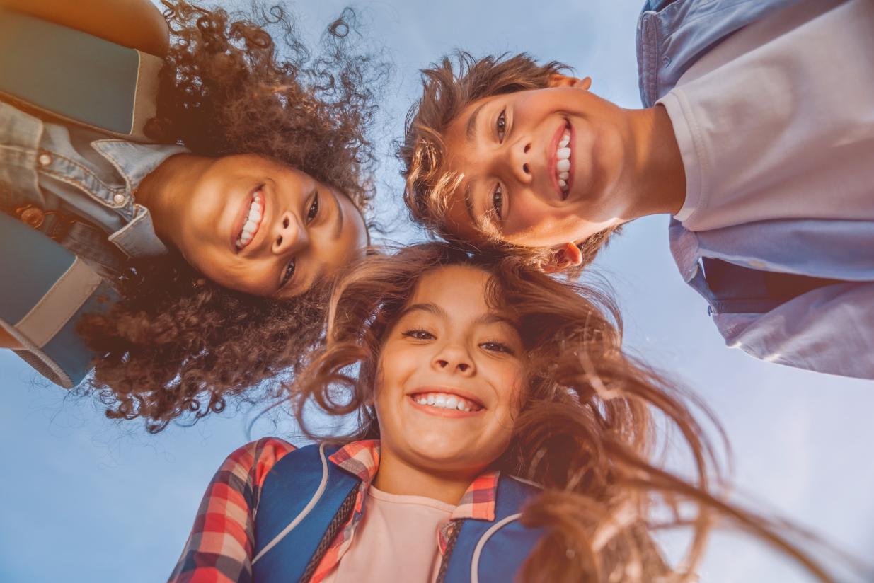 three kids with their heads together looking down at the camera and smiling