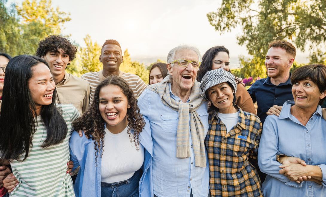 Multigenerational group of smiling people gathered together outdoors.